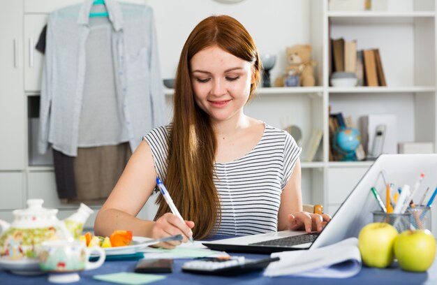 Young woman is sitting with laptop and documents at the table