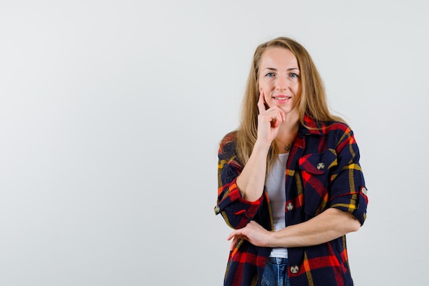 The young woman is smiling by putting her forefinger on cheek on white background