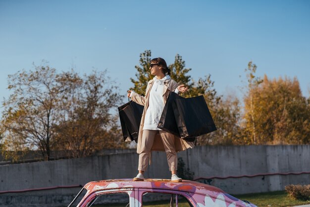 A young woman is standing in a car with bags in her hands