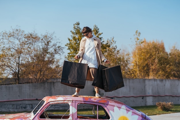 A young woman is standing in a car with bags in her hands