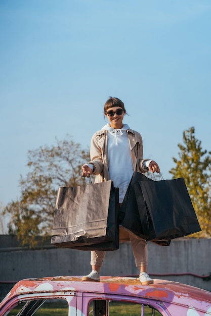 A young woman is standing in a car with bags in her hands