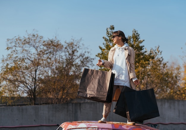 A young woman is standing in a car with bags in her hands