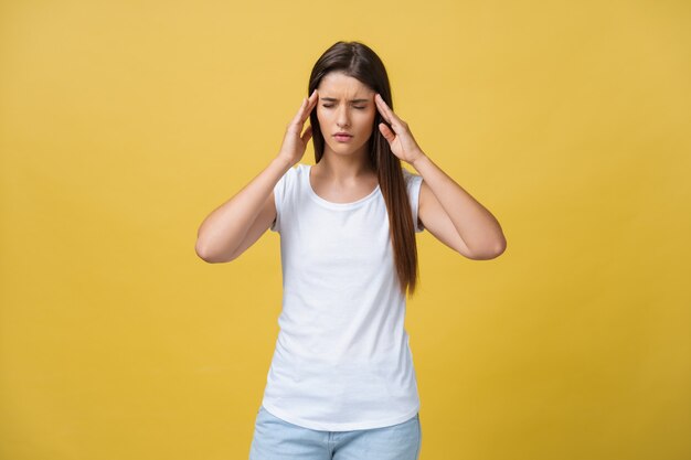 Young woman is suffering from a headache against a yellow background. Studio shot.