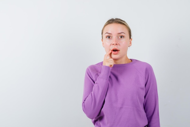 The young woman is suprising by holding her finger on lip on white background