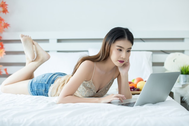 A young woman is watching a movie from a laptop on the bed at home
