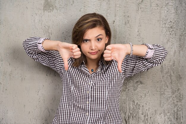 Foto gratuita giovane donna isolata sulla parete scura che mostra i pollici verso il basso con due mani