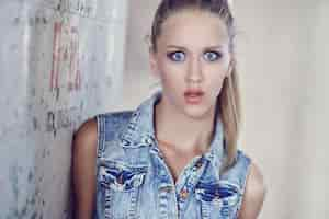 Free photo young woman in jeans jacket posing near concrete wall.