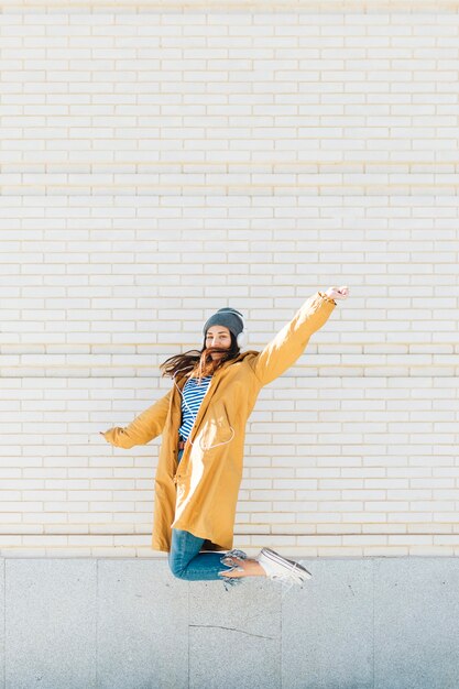 young woman jumping against brick wall wearing headset