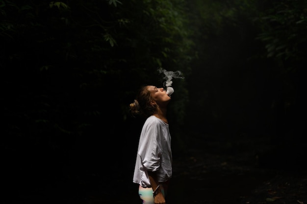 A young woman in the jungle lets out puffs of smoke Vape