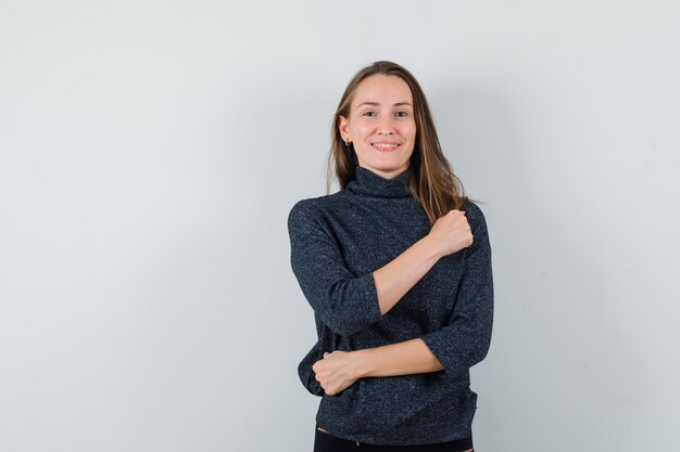 Young woman keeping clenched fist on chest in shirt and looking confident. front view.