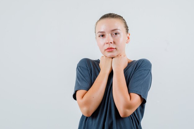 灰色のTシャツで顎の下に拳を保ち、心配そうに見える若い女性