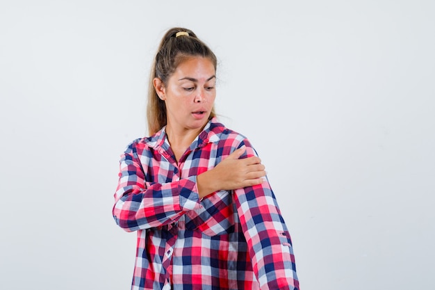 Young woman keeping hand on her arm in casual shirt and looking focused , front view.