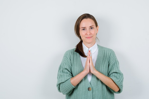 Foto gratuita giovane donna che tiene le mani nel gesto di preghiera in camicetta, cardigan e sembra sensata. vista frontale.