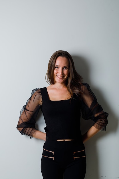 Young woman keeping hands behind waist and smiling gracefully in black blouse and black pants and looking charming