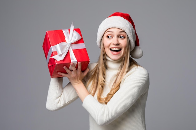 Young woman keeps a christmas gift in white paper isolated gray wall