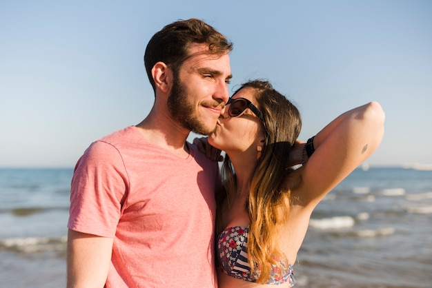 Free photo young woman kissing her boyfriend at beach