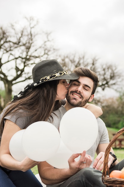 Young woman kissing her boyfriend holding white balloons in hand