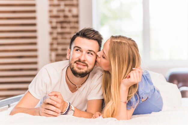 Young woman kissing her boyfriend lying on bed in the bedroom