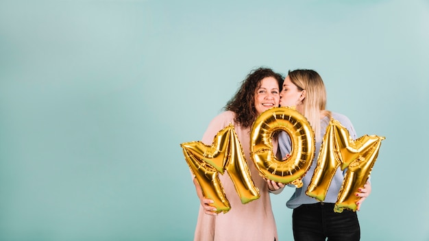 Young woman kissing mom while holding balloons