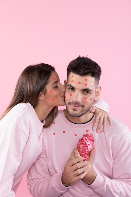 Молодая женщина целует улыбающегося человека с бумажными сердечками на лицах