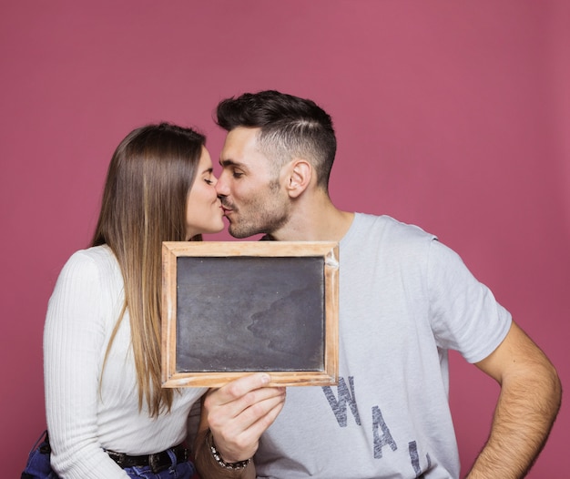 Young woman kissing with positive man and showing photo frame