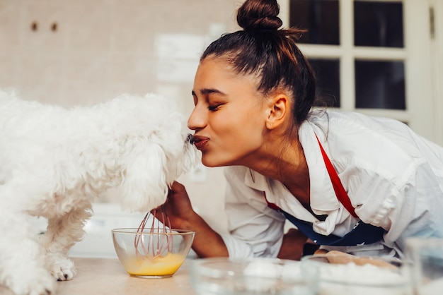 キッチンで若い女性がかわいい白いマルチーズ犬にキスをする