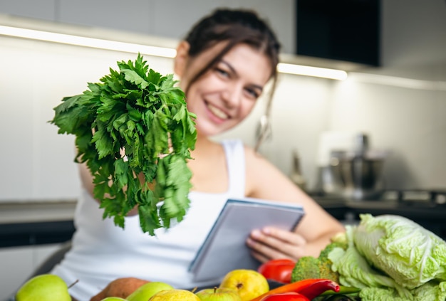 Free photo a young woman in the kitchen with a notepad and parsley in her hand