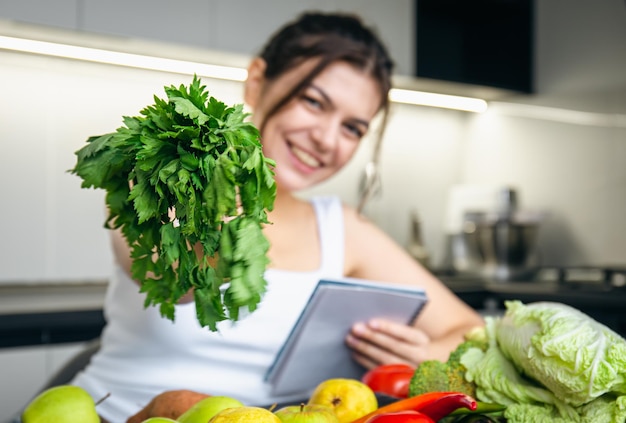 Foto gratuita una giovane donna in cucina con un blocco note e prezzemolo in mano