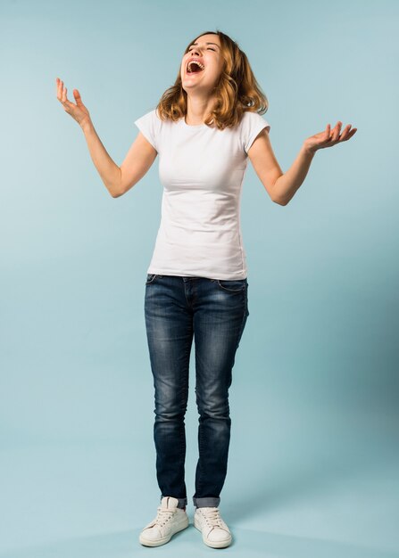 Young woman laughing loudly against blue background