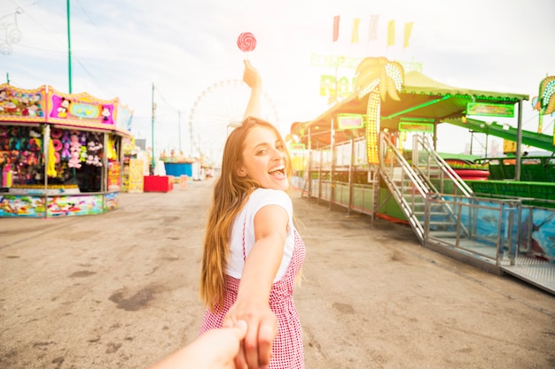 Young woman leading her friend holding lollipop at amusement park