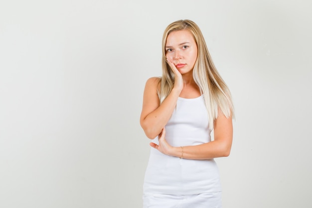 Young woman leaning cheek on hand in singlet, mini skirt and looking sad 