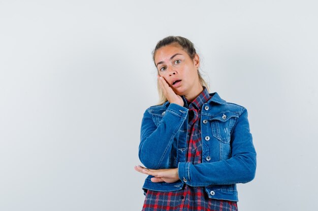 Young woman leaning cheek on palm in shirt, jacket and looking pensive , front view.