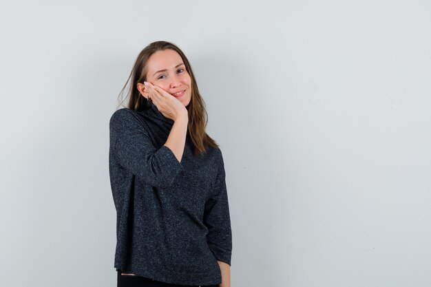 Young woman leaning cheek on palm in shirt and looking cute. front view.