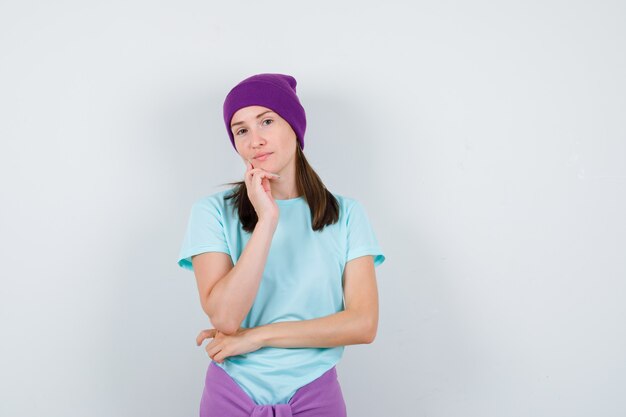 青いTシャツ、紫色のビーニーで手に顎をもたれ、真剣に見える若い女性、正面図。