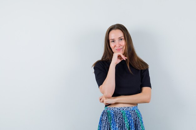 Young woman leaning chin on hand and posing at camera in black t-shirt and blue skirt and looking attractive