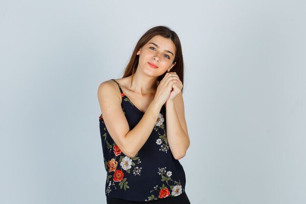 Young woman leaning on clasped hands as pillow in blouse and looking cheery , front view.