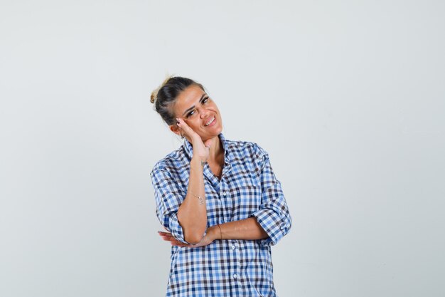 Young woman leaning on hand in checkered shirt and looking happy.