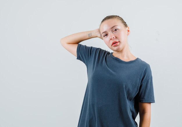 Young woman leaning head on raised palm in grey t-shirt and looking confident