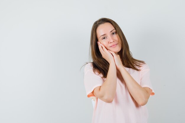 ピンクのTシャツの枕として手のひらに寄りかかって素敵に見える若い女性。