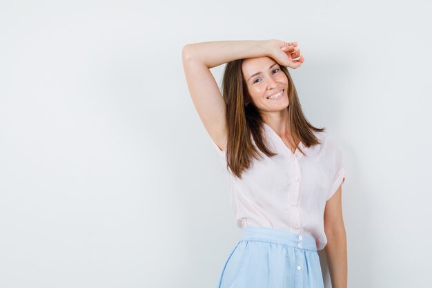 Young woman leaning raised arm on head in t-shirt, skirt and looking happy. front view.