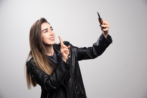 Молодая женщина в кожаной куртке, делающая селфи со своим мобильным телефоном