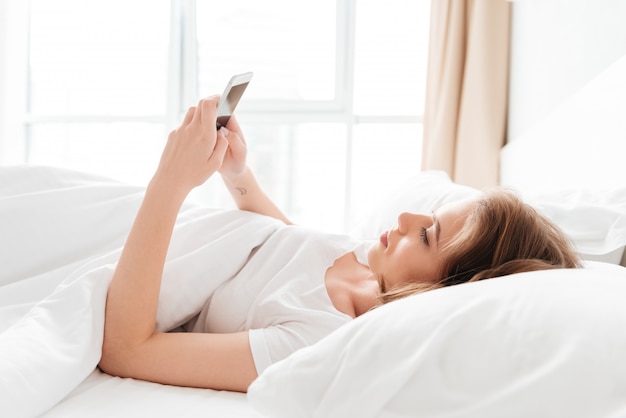 young woman lies in bed looking aside chatting