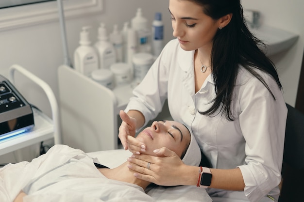 Молодая женщина лежит с закрытыми глазами, косметолог делает процедуру