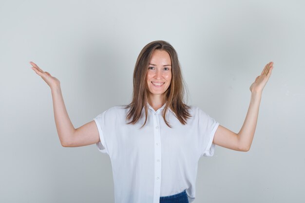 Young woman lifting arms up in white t-shirt, jeans and looking cheerful