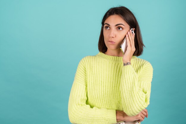 Young woman in light green sweater with mobile phone having conversation listening audio message