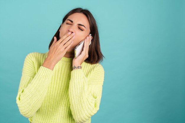 Young woman in light green sweater with mobile phone having conversation listening audio message