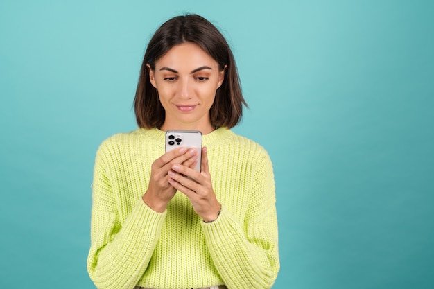 笑顔のタイピングメッセージと携帯電話と薄緑色のセーターの若い女性