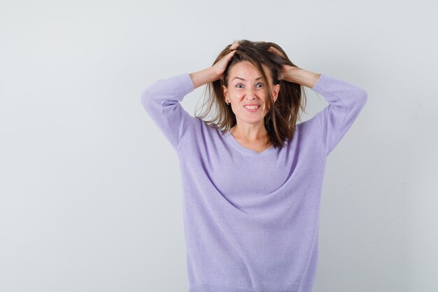 Young woman in lilac blouse holding hands on her head and looking complicated 