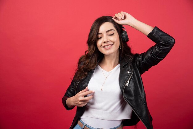 Young woman listening music in headphones and dancing on a red background. High quality photo