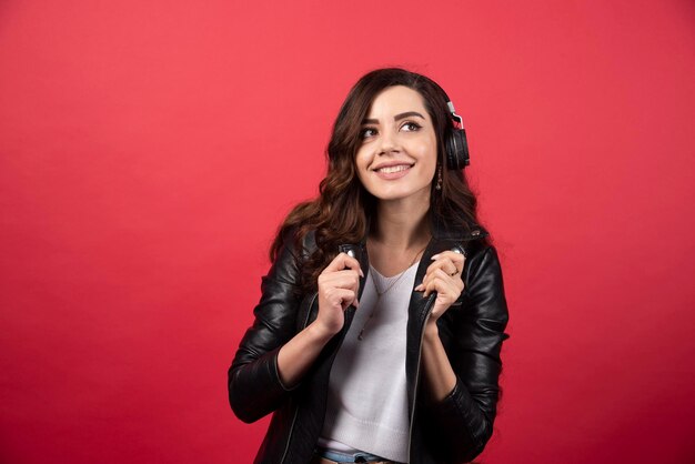 Young woman listening music in headphones and posing on a red background. High quality photo